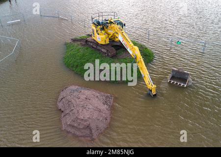 Upton-upon-Severn, Worcestershire, 12. Januar 2023 - Eine kleine Stadt in Worcestershire wurde überschwemmt, nachdem der Fluss Severn seine Ufer aufgrund steigender Wasserstände platzte. Ein Abfallverwertungszentrum wurde geschlossen, ebenso wie eine örtliche Zufahrtsstraße, die Hanley Road, die vom gemeinderat geschlossen wurde. Ein großer gelber Bagger wurde auch auf einem kleinen grasbewachsenen Hügel gesehen, als die Überschwemmung ihn umgab. Quelle: Stop Press Media/Alamy Live News Stockfoto