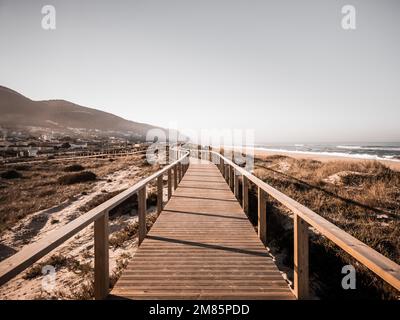 Eine lange Promenade auf einer grasbedeckten Sanddüne entlang des Strandes, die zum Berg mit entsättigten Farben führt. Das Konzept der Zukunft. Quiaios Beach, Portugal Stockfoto