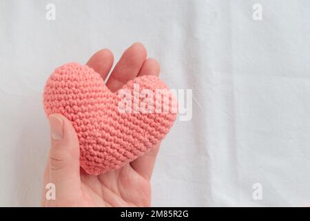 Gehäckseltes Amigurumi-rosa Herz in der Hand einer Frau. Valentinstag-Banner mit einem Werbespot Stockfoto