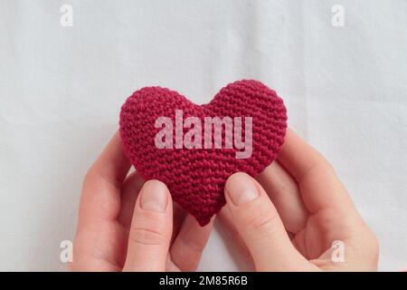 Gehäckseltes Amigurumi-Purpurherz in den Händen einer Frau. Valentinstag-Banner mit einem Werbedruckraum, Draufsicht Stockfoto