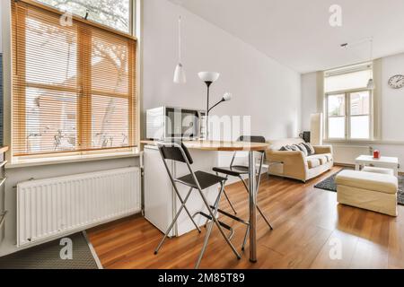 Ein Wohnzimmer mit Holzfußboden und weißen Wänden, einschließlich eines kleinen Esstisches vor dem Fenster Stockfoto