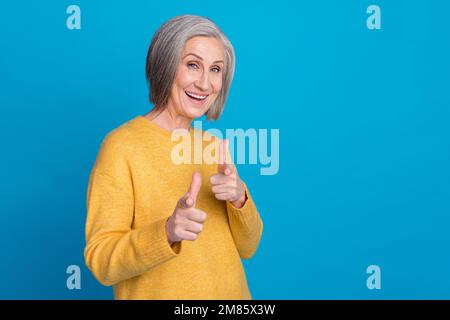 Fotoporträt der umwerfenden Großmutter Finger zeigen coole, energiegeladene Promoter Tragen trendiges gelbes Outfit isoliert auf blauem Hintergrund Stockfoto