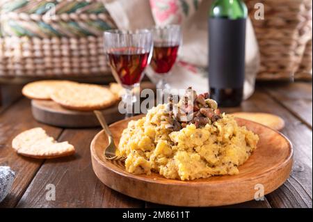 Cremige Polenta mit Porcini-Pilzen und Speck, serviert auf dunklem Holzhintergrund mit einem Glas Rotwein. Typisch norditalienische Küche, Trentino in den Alpen Stockfoto