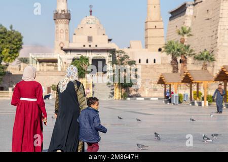 LUXOR, ÄGYPTEN - 27. Dez. 2022. Zwei Frauen und ein Kind auf dem Rücken laufen Tag für Tag, um in der Moschee in einer arabischen Stadt am blauen Himmel zu beten Stockfoto