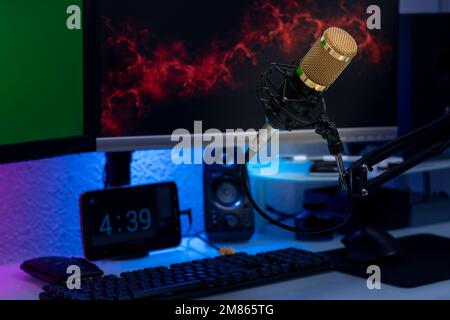 Kondensatormikrofon im Gamer-Setup mit Monitoren, Tastatur, Maus und farbigen Lichtern. Stockfoto