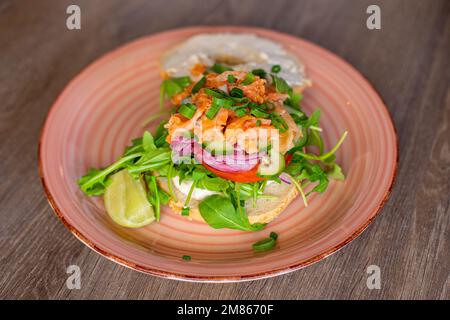 Teller mit köstlichem Lachsburger auf Holztisch. Servieren Sie ein gesundes Sandwich zum Frühstück. Europäische Küche, ausgewogen Stockfoto