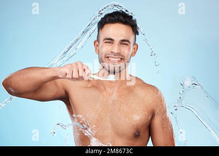 Gesicht, Wasserspritzer und Mann mit Zahnbürste zur Reinigung im Studio auf blauem Hintergrund. Zahnverblendungen, Hygiene und Porträt des glücklichen männlichen Modells Stockfoto