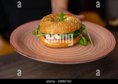 Teller mit saftigem, leckeren veganen Burger, isoliert auf Holztisch. Zum Abendessen wird ein herzhaftes warmes Sandwich serviert. Fast Food Cafe Stockfoto