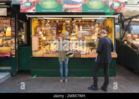 Bozen Markt, Blick auf Menschen, die Speisen an einem Verkaufsstand kaufen, der sich auf lokale Fleisch- und Käsesorten spezialisiert hat, auf dem Piazza Erbe Markt, im Stadtzentrum von Bozen, Italien Stockfoto