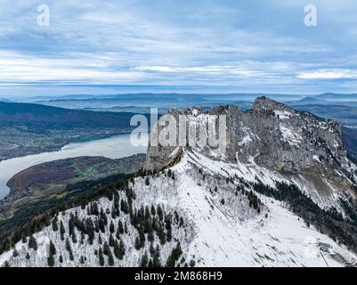 Drohnenaufnahme der Bergkette mit Schnee in der Nähe des Sees unter bewölktem Himmel Stockfoto