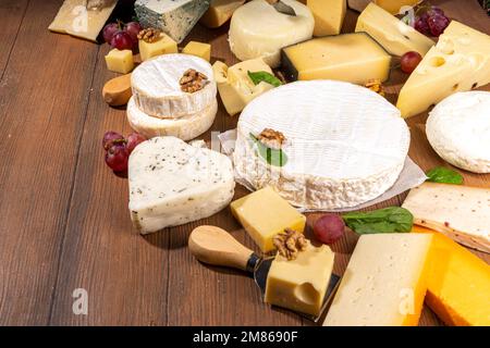 Verschiedene Käsesorten. Käseplatte mit verschiedenen Käse, mit Trauben, Nüssen, Käsemesser und Gewürzen, Holzhintergrund Kopierraum Stockfoto