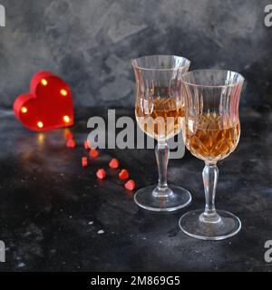 Zwei Gläser Rosenlimonade und ein rot beleuchtetes Herz auf dunklem Hintergrund Stockfoto