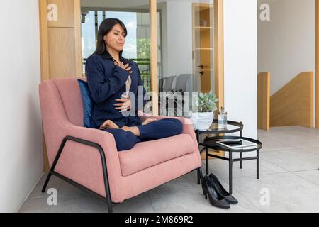 Frau, die in einer Lotusblume auf einem Sessel im Büro sitzt, während sie an einem Arbeitstag eine Pause macht. Stockfoto