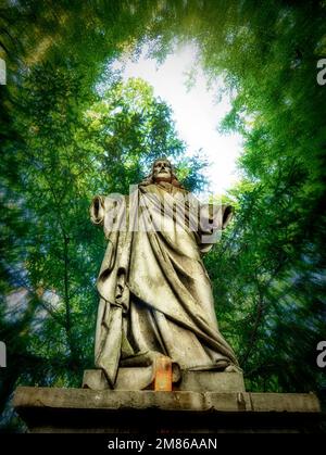 Alte beschädigte Steinstatue von Jesus Christus / Jesus von Nazareth fotografiert in einem Holz. Stockfoto