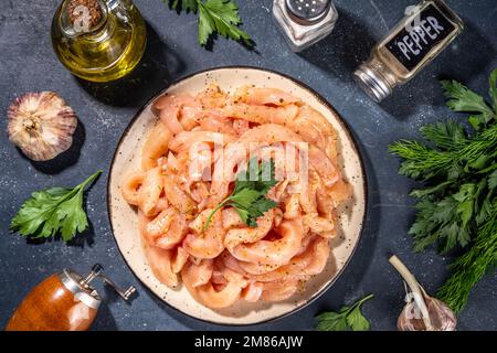 Hintergrund der Kochdiät für weißes Geflügelfleisch. Frisch geschnittene Hähnchenstreifen roh zum Kochen, mit Gewürzen, Kräutern, auf schwarzem Betonhintergrund, Draufsicht C. Stockfoto