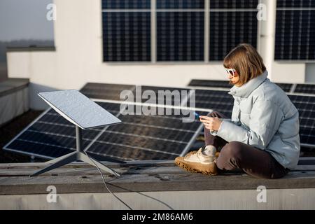 Frau benutzt Starlink Internet auf dem Dach mit Solarpaneelen Stockfoto