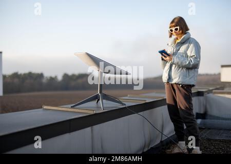 Eine Frau mit Telefon benutzt Starlink-Satelliten-Internet auf dem Dach Stockfoto