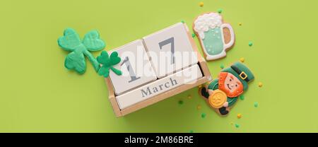 Klee mit leckeren Lebkeksen und Kalender mit Datum von St. Patrick's Day auf grünem Hintergrund Stockfoto