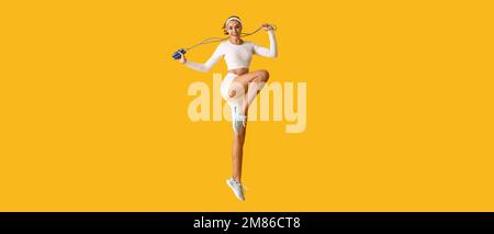Sportliche, hüpfende junge Frau mit Seilspringen auf gelbem Hintergrund Stockfoto