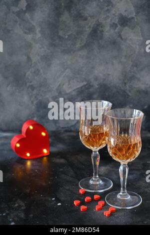 Zwei Gläser Rosenlimonade und ein rot beleuchtetes Herz auf dunklem Hintergrund Stockfoto