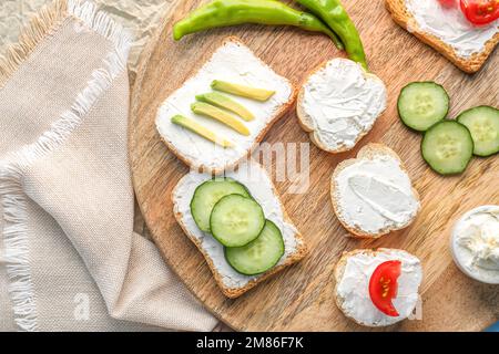 Holzbrett mit leckeren Sandwiches mit Frischkäse und Gemüse, Nahaufnahme Stockfoto