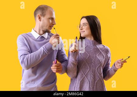 Ein junges Paar mit elektronischen Einweg-Zigaretten auf gelbem Hintergrund Stockfoto