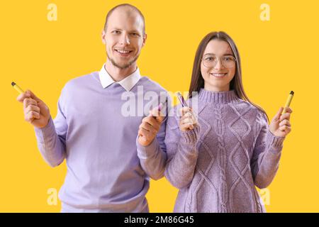 Ein junges Paar mit elektronischen Einweg-Zigaretten auf gelbem Hintergrund Stockfoto