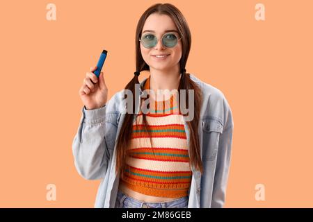 Junge Frau in Sonnenbrille mit elektronischer Einweg-Zigarette auf beigefarbenem Hintergrund Stockfoto