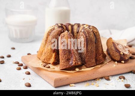 Holzbrett mit köstlichem Kuchen und verstreuten Kaffeebohnen auf hellem Hintergrund, Nahaufnahme Stockfoto