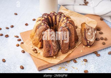 Holzbrett mit köstlichem Kuchen und verstreuten Kaffeebohnen auf hellem Hintergrund Stockfoto