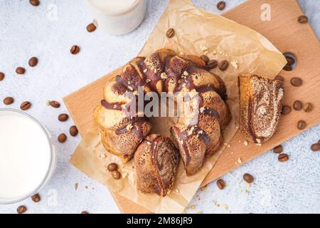 Holzbrett mit köstlichem Kuchen und verstreuten Kaffeebohnen auf hellem Hintergrund Stockfoto