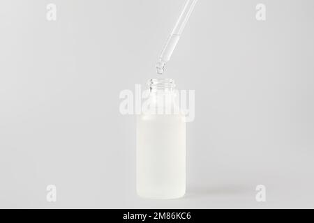 Tropfen von natürlichem Serum aus der Pipette in die Flasche auf hellem Hintergrund Stockfoto