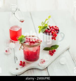 Sommergetränk mit weißem Sekt. Hausgemachter erfrischender Fruchtcocktail oder Punsch mit Champagner, roter Johannisbeere, Eiswürfeln und Minzblättern auf Weiß Stockfoto