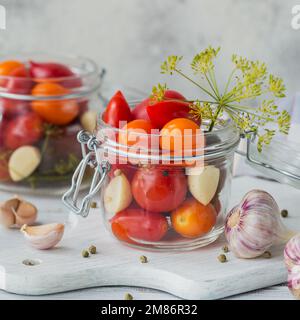 Frische und eingelegte Tomaten, Gewürze und Knoblauch auf einem weißen Holztisch. Gesunde fermentierte Nahrung. Gemüse aus Hauskonserven. Stockfoto