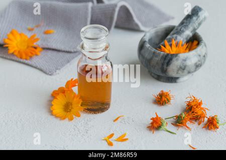 Calendula-Produkte. Flasche mit kosmetischem, aromatischem oder ätherischem Öl und frischen und trockenen Calendula-Blüten auf hellem Hintergrund. Aromatherapie, Spa und Stockfoto