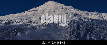 Ein majestätischer und schneebedeckter Berg steht hoch vor einem klaren blauen Himmel und bietet einen atemberaubenden Panoramablick. Stockfoto
