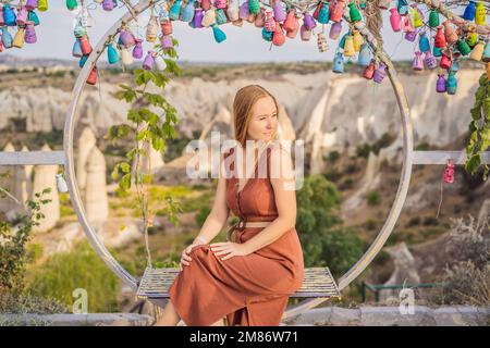 Junge Frau, die das Tal mit Felsformationen und Feenhöhlen in der Nähe von Goreme in Kappadokien, Türkei, erkundet. Wunschbaum. Kleine mehrfarbige Kannen mit Stockfoto