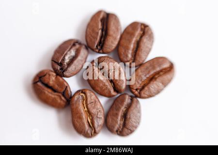 Mehrere Körner gerösteten Kaffees auf weißem Hintergrund. Makro. Fotografiert mit einer alten Linse mit unscharfen Kanten und mit geringer Tiefe Stockfoto