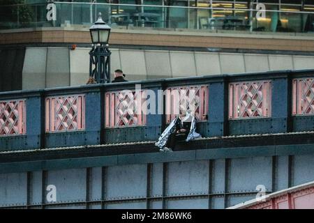 London, Großbritannien. 12. Januar 2023. Die Frau ist auf dem äußeren Rand der Brücke zu sehen, mit einer großen Präsenz von Sanitätern, Rettungsdiensten, Polizei und anderen anwesenden Personen auf der Brücke hinter der Brücke sowie auf der Themse. Die Lambeth Bridge in Westminster war für mehrere Stunden heute Nachmittag und Abend geschlossen, als eine Frau über das Geländer geklettert war, mit der Absicht, in den Fluss zu springen. Während Polizeirettungsdienste den Fluss patrouillierten, fuhren Fracht- und einige Passagierboote weiter darunter. Kredit: Imageplotter/Alamy Live News Stockfoto