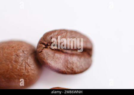 Mehrere Körner gerösteten Kaffees auf weißem Hintergrund. Makro. Fotografiert mit einer alten Linse mit unscharfen Kanten und mit geringer Tiefe Stockfoto