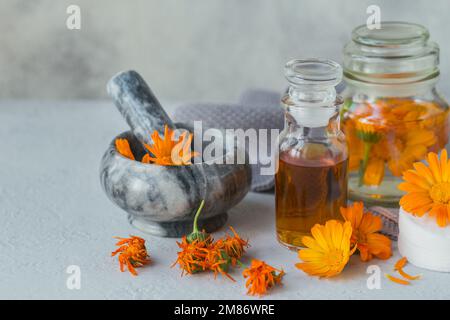 Calendula-Produkte. Flasche mit kosmetischem, aromatischem oder ätherischem Öl und frischen und trockenen Calendula-Blüten auf hellem Hintergrund. Aromatherapie, Spa und Stockfoto