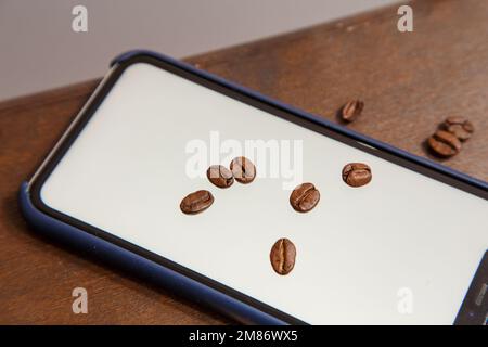 Der Türke steht auf einem Laptop, Kaffeebohnen sind überall verstreut und ein Telefon mit einer weißen Farbe im Inneren. Hochwertiges Foto Stockfoto