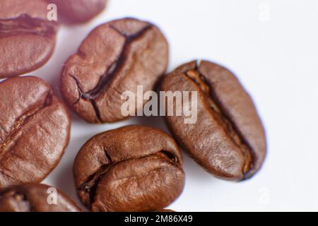 Mehrere Körner gerösteten Kaffees auf weißem Hintergrund. Makro. Fotografiert mit einer alten Linse mit unscharfen Kanten und mit geringer Tiefe Stockfoto