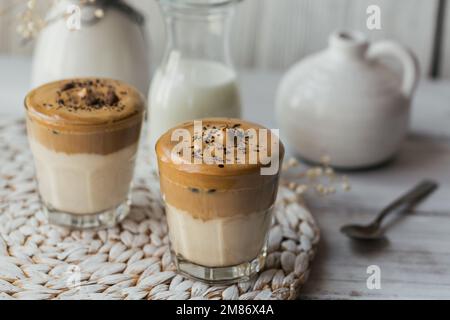 Ein Glas Iced Dalgona Kaffee, trendiger, flauschiger, cremiger Schlagsahne Kaffee und Milch auf weißem Holzhintergrund. Stockfoto