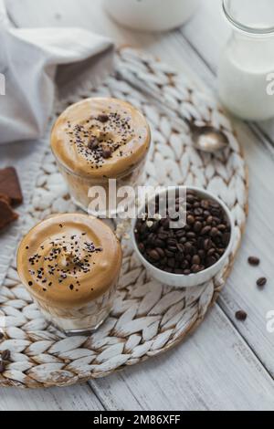 Dalgona schlug Kaffee, Instant, Sahne, Eiskaffee. Cocktail mit Kaffee, Milch und Eiswürfeln auf einem Modell mit hellem Hintergrund. Trendiger Hintergrund für Drinks Stockfoto