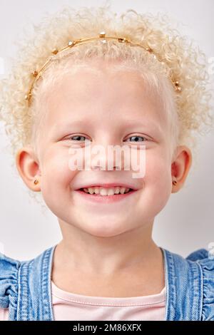 Glückliches, weißes Mädchen hat ein breites Lächeln, zeigt perfekte Zähne auf weißem Studiohintergrund. Weiße Locken und blaue Augen. Fröhlich aufgeregtes Kinderklo Stockfoto