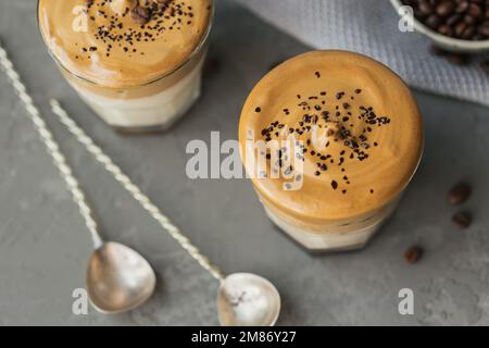 Ein Glas Iced Dalgona Kaffee, trendiger, flauschiger, cremiger Schlagsahne Kaffee und Milch auf grauem Hintergrund. Stockfoto