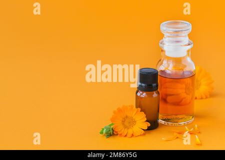 Flaschen mit Topf-Ringelminze-Tinktur oder -Infusion und ätherischem Öl mit frischen Calendula-Blüten auf orangefarbenem Hintergrund. Natürliche pflanzliche Alternative Stockfoto