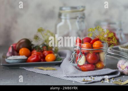 Aufbewahrung frischer und eingelegter Tomaten, Gewürze und Knoblauch auf grauem Betontisch. Gesunde fermentierte Nahrung. Gemüse aus Hauskonserven. Stockfoto