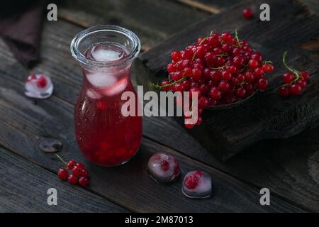 Sommergetränk mit weißem Sekt. Hausgemachter erfrischender Fruchtcocktail oder Punsch mit Champagner, roter Johannisbeere, Eiswürfeln und Minzblättern im Dunkeln Stockfoto